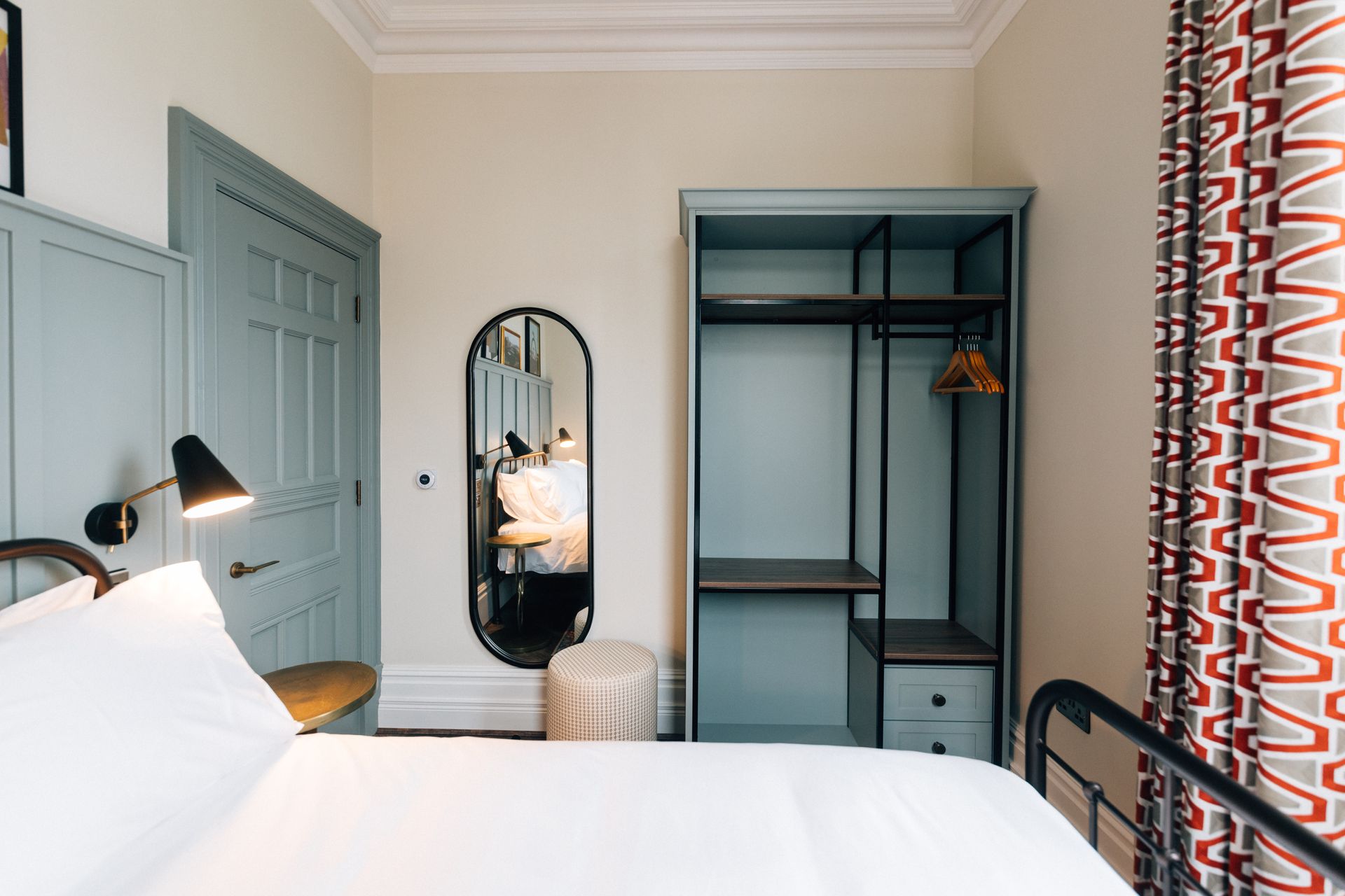 Bedroom with a light blue door, closet, and walls. A black bed frame, mirror, and lamp are visible.