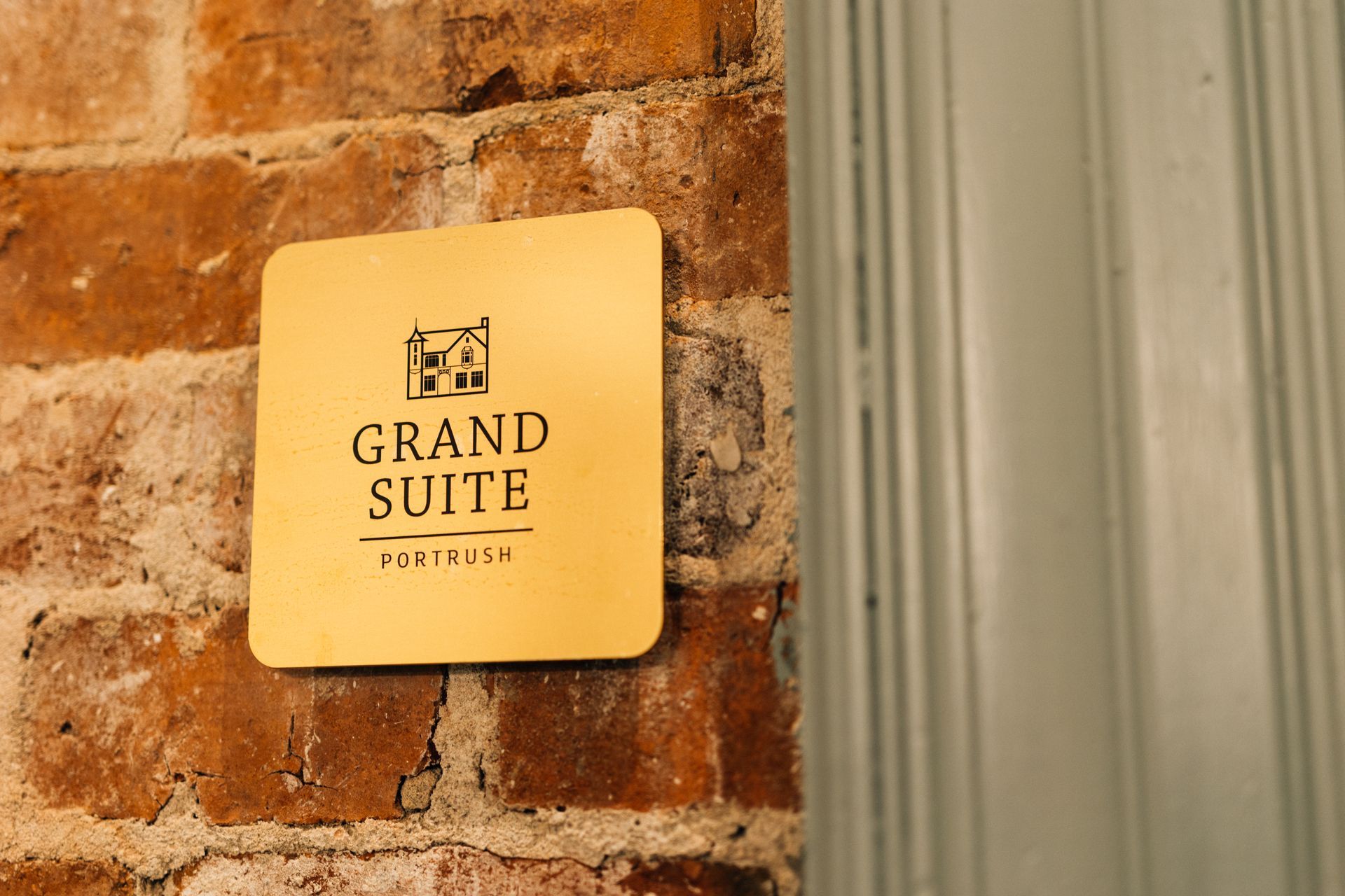 Gold “Grand Suite” sign on a brick wall beside a door frame.