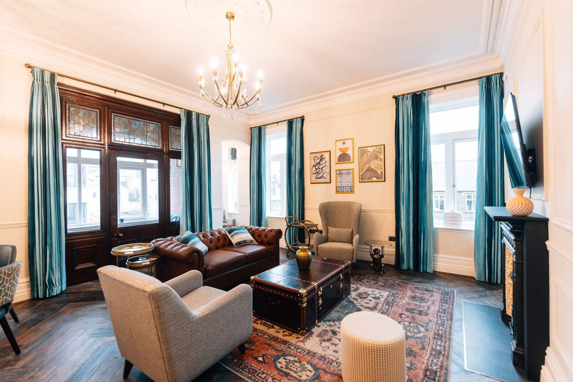 Luxurious living room with brown leather sofa, teal curtains, ornate trim, and chandelier.