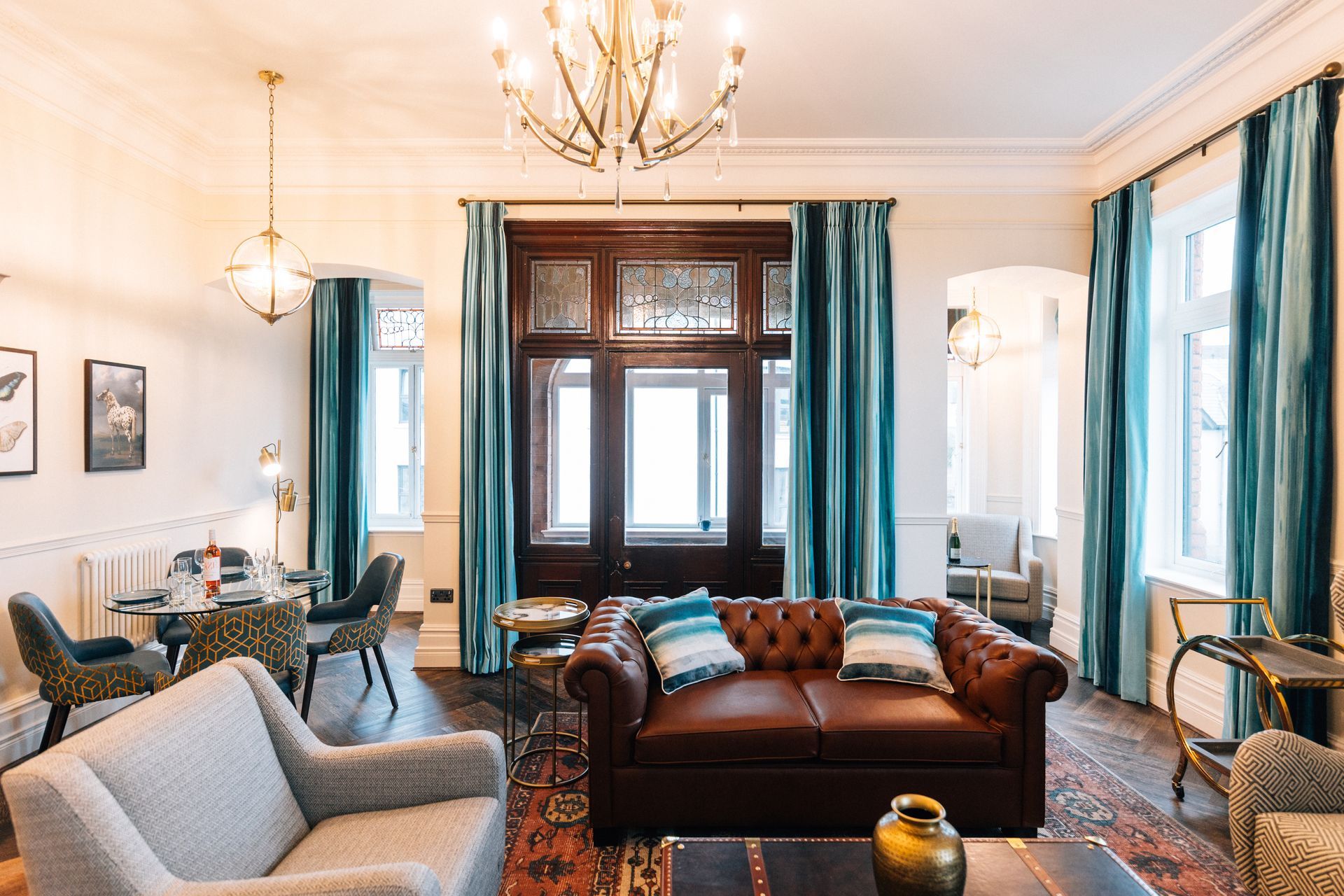 A luxurious living room with a brown leather couch, teal curtains, and a decorative stained-glass door.