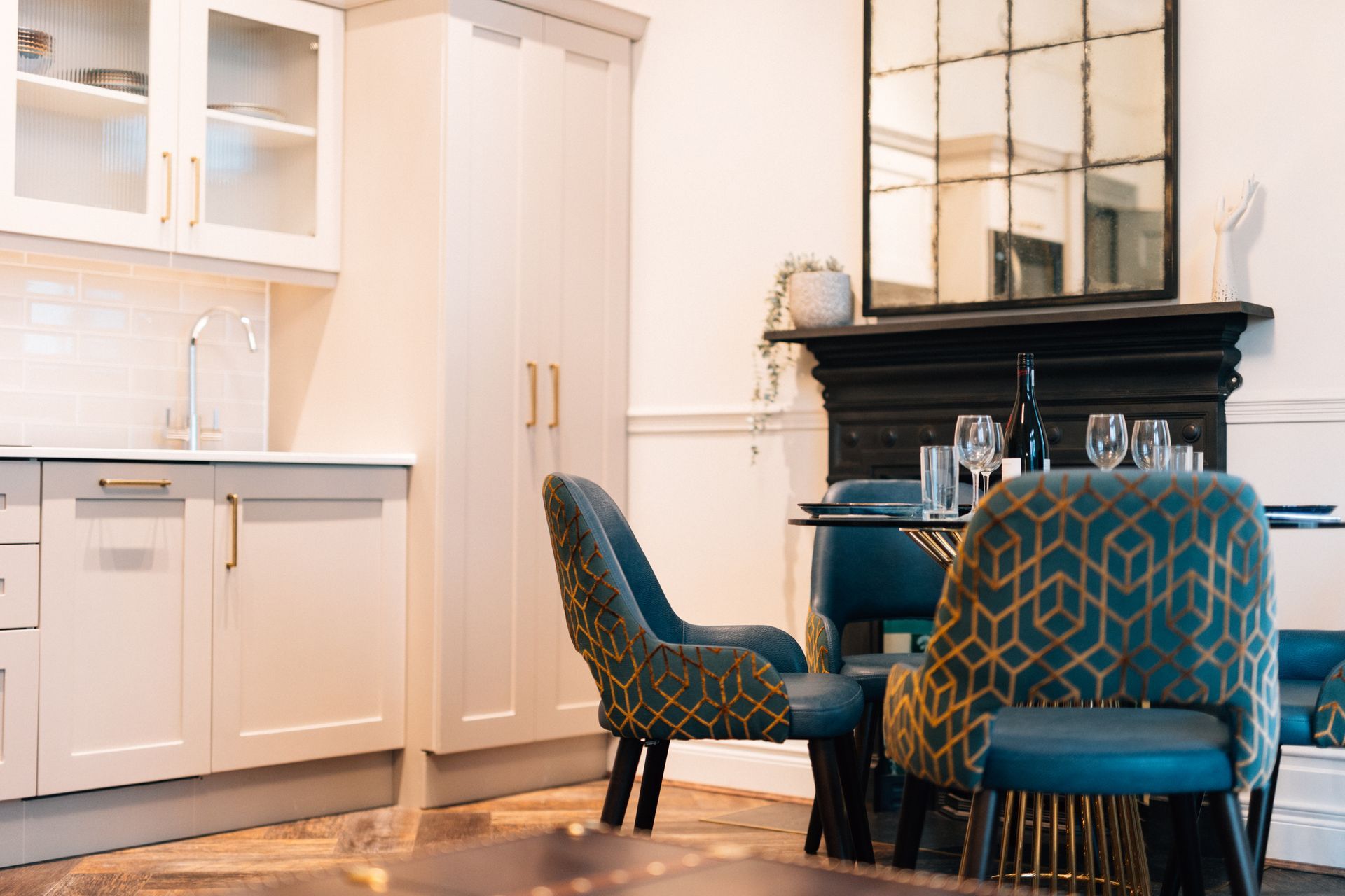 Kitchen and dining area with white cabinets, blue chairs, and a mirror above a fireplace.