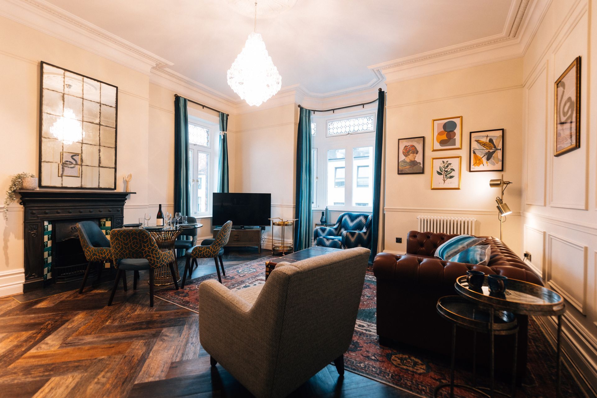 Living room with herringbone floors, leather sofa, dining table, and a large mirror above the fireplace.
