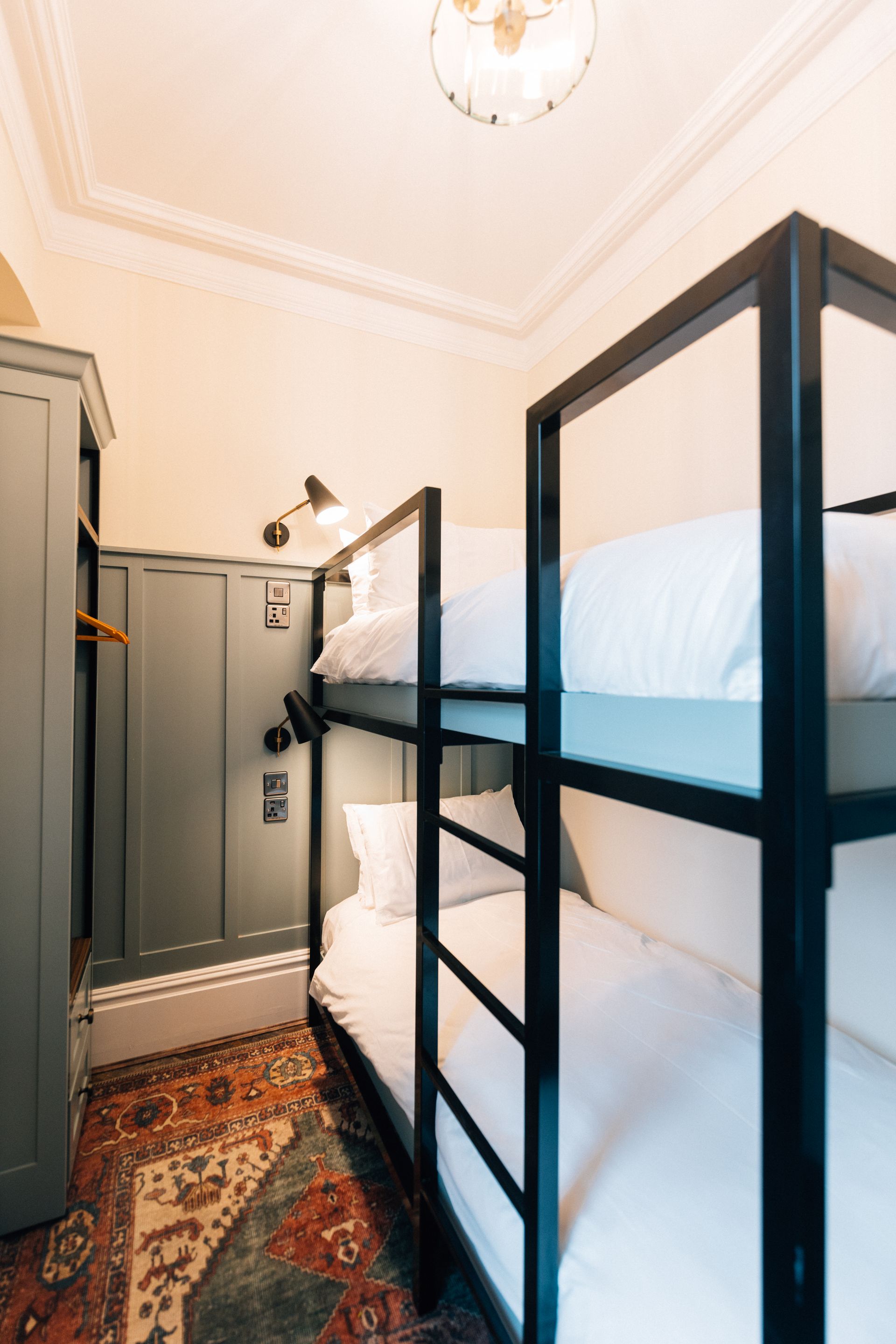 Bunk beds in a small room with dark grey walls, patterned rug, and a small reading lamp.
