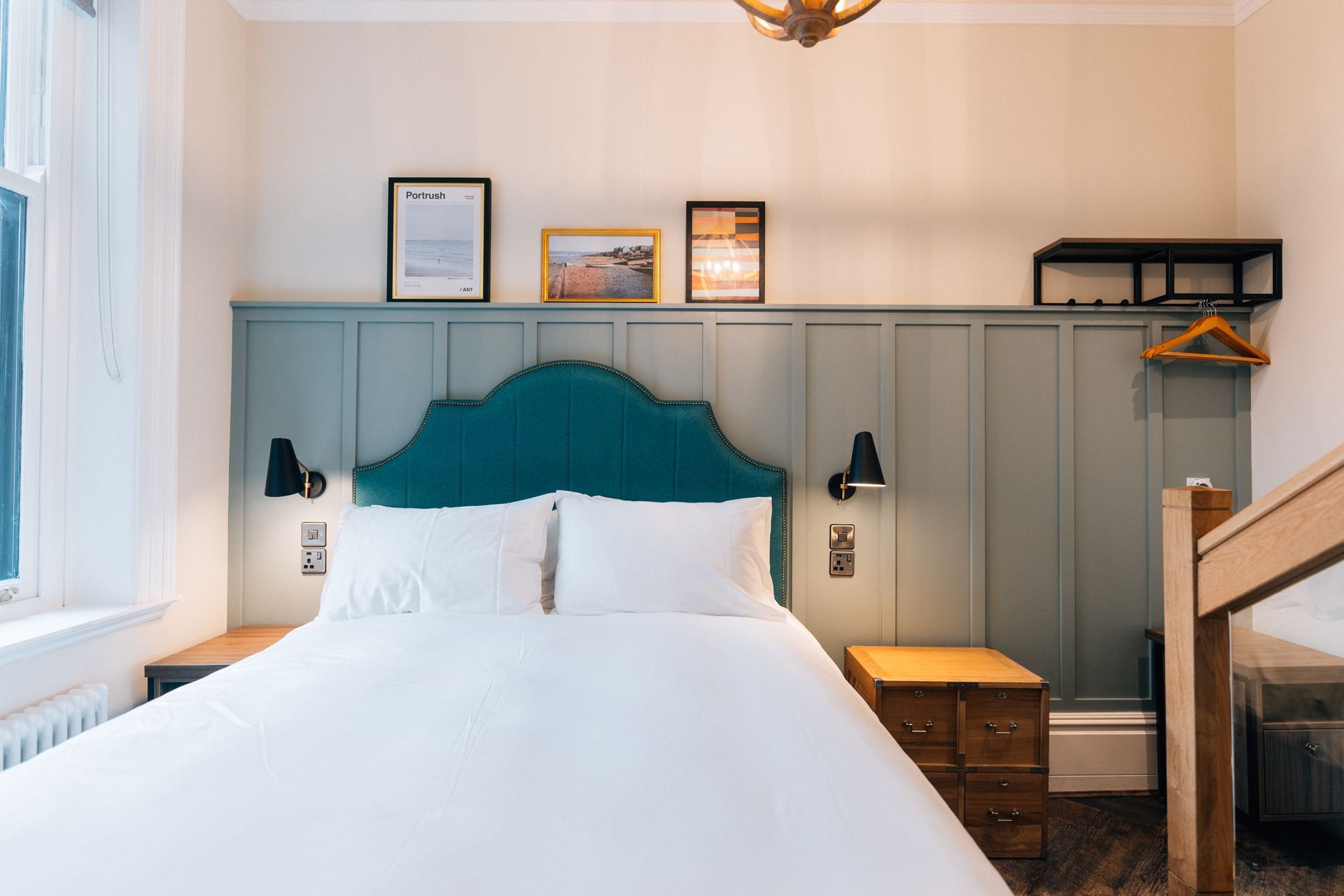 A hotel bedroom featuring a bed with a teal headboard, framed artwork, and two nightstands.