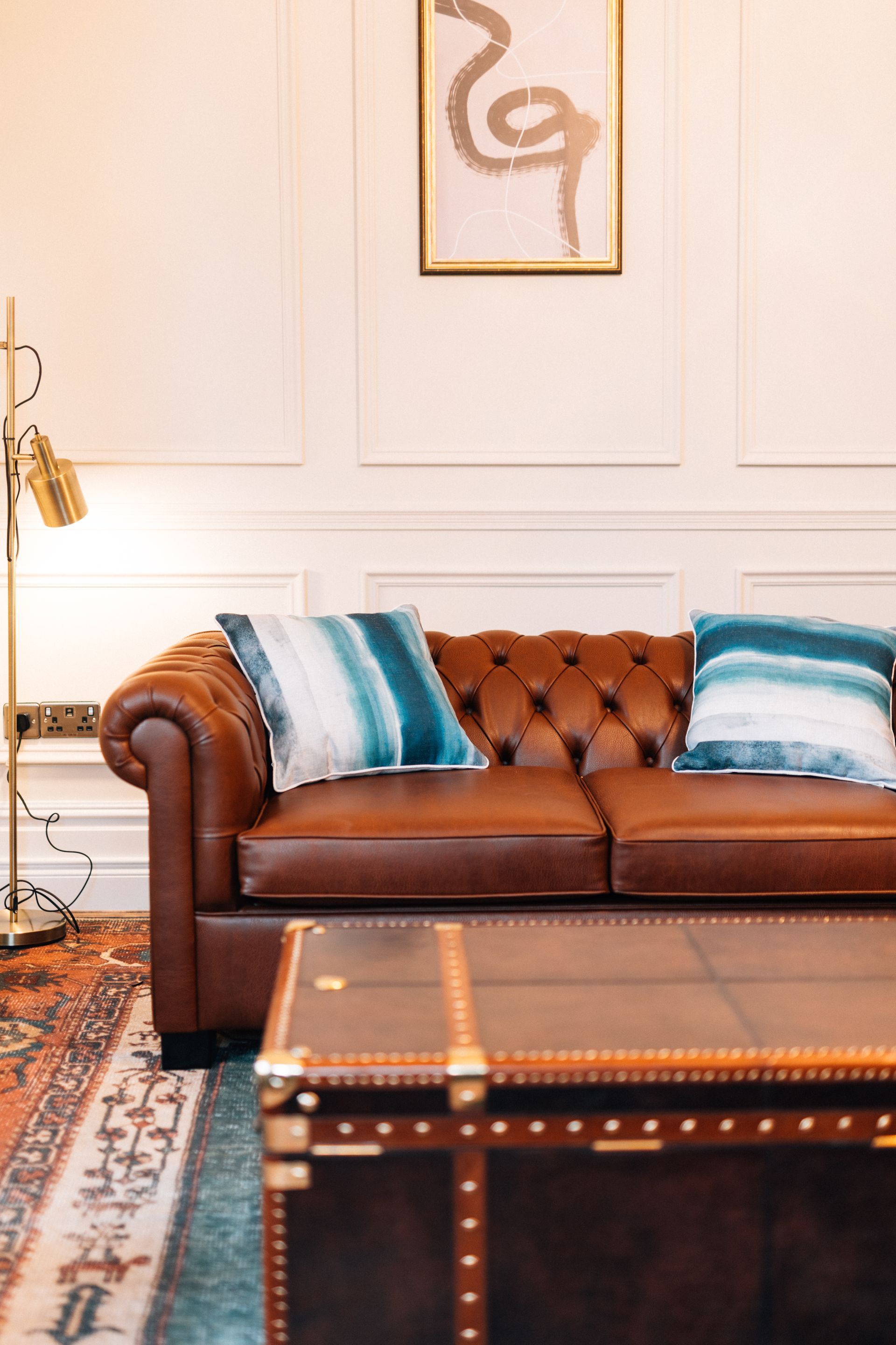 Brown leather Chesterfield sofa with turquoise pillows, coffee table, and artwork in a room
