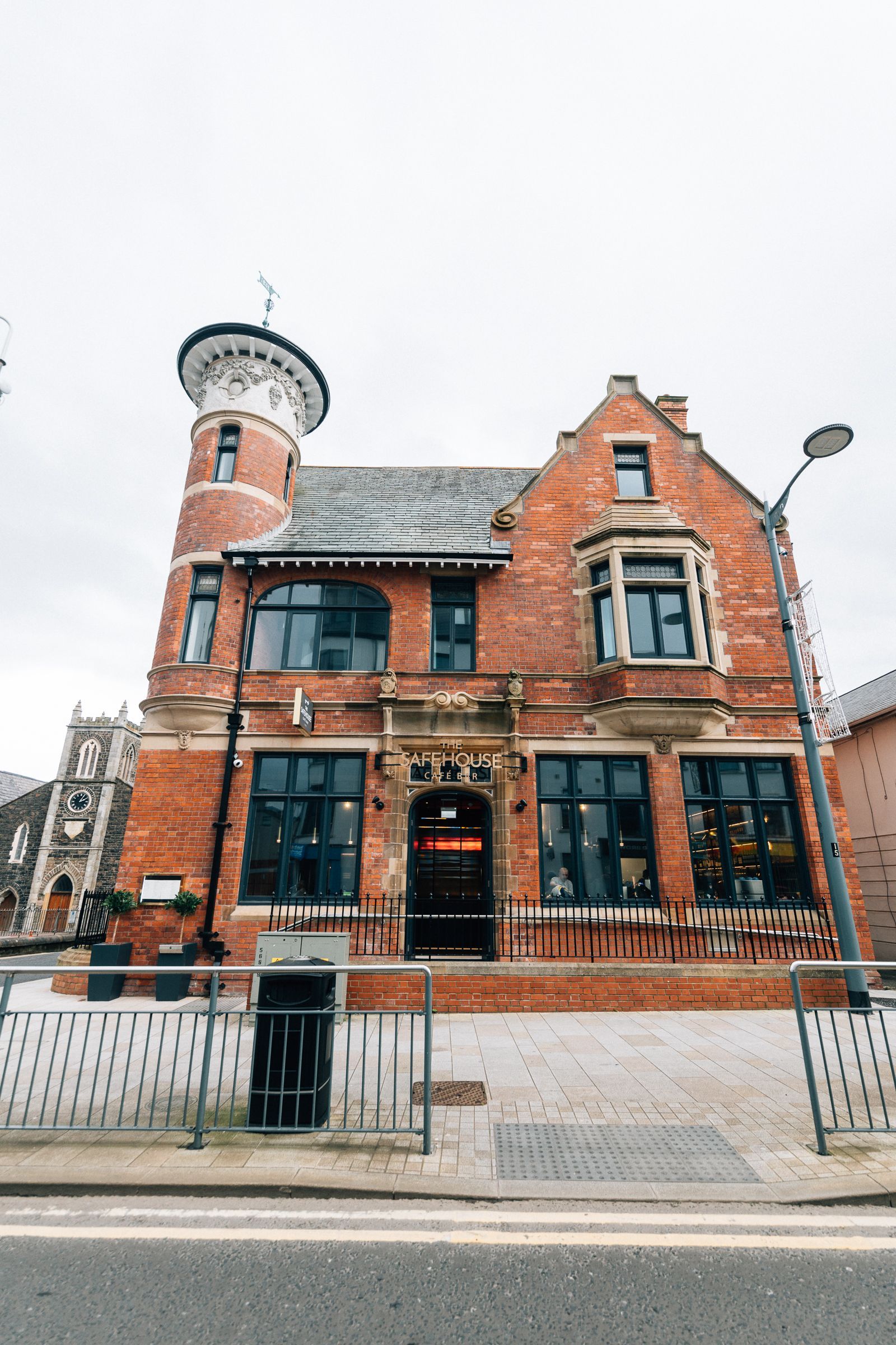 Red brick building with tower, black-framed windows, and a decorative entrance. Street view on an overcast day.