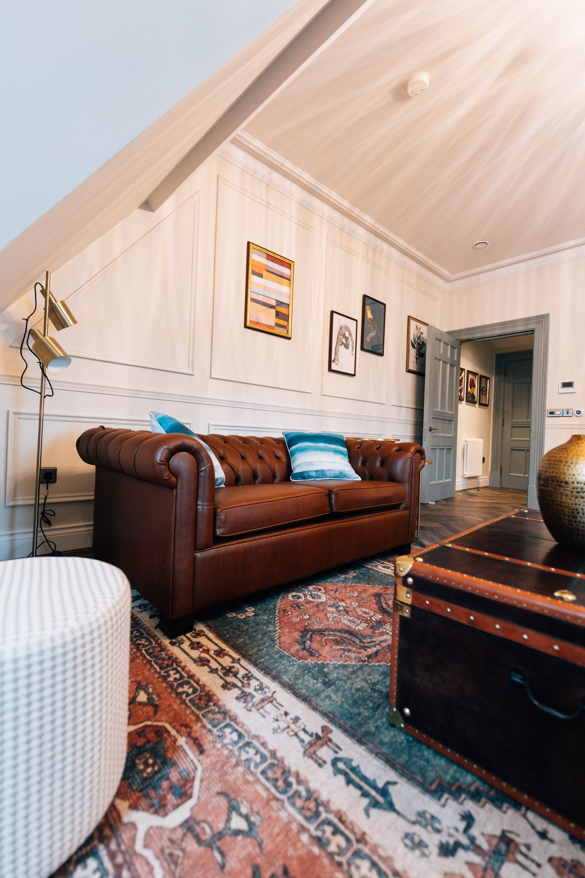 Cozy attic living room with brown leather sofa, patterned rug, trunk table, and sloped wood ceiling