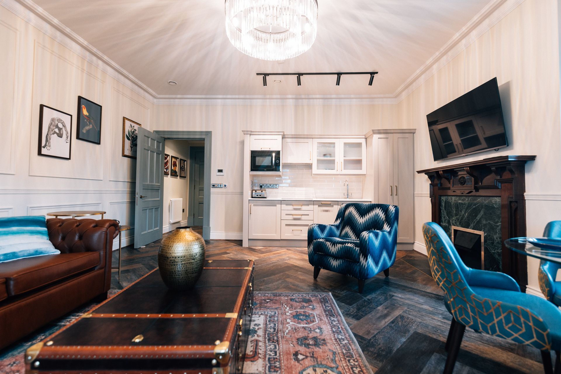 A luxurious living room with a kitchen, including a leather sofa, patterned chair, fireplace, and TV.