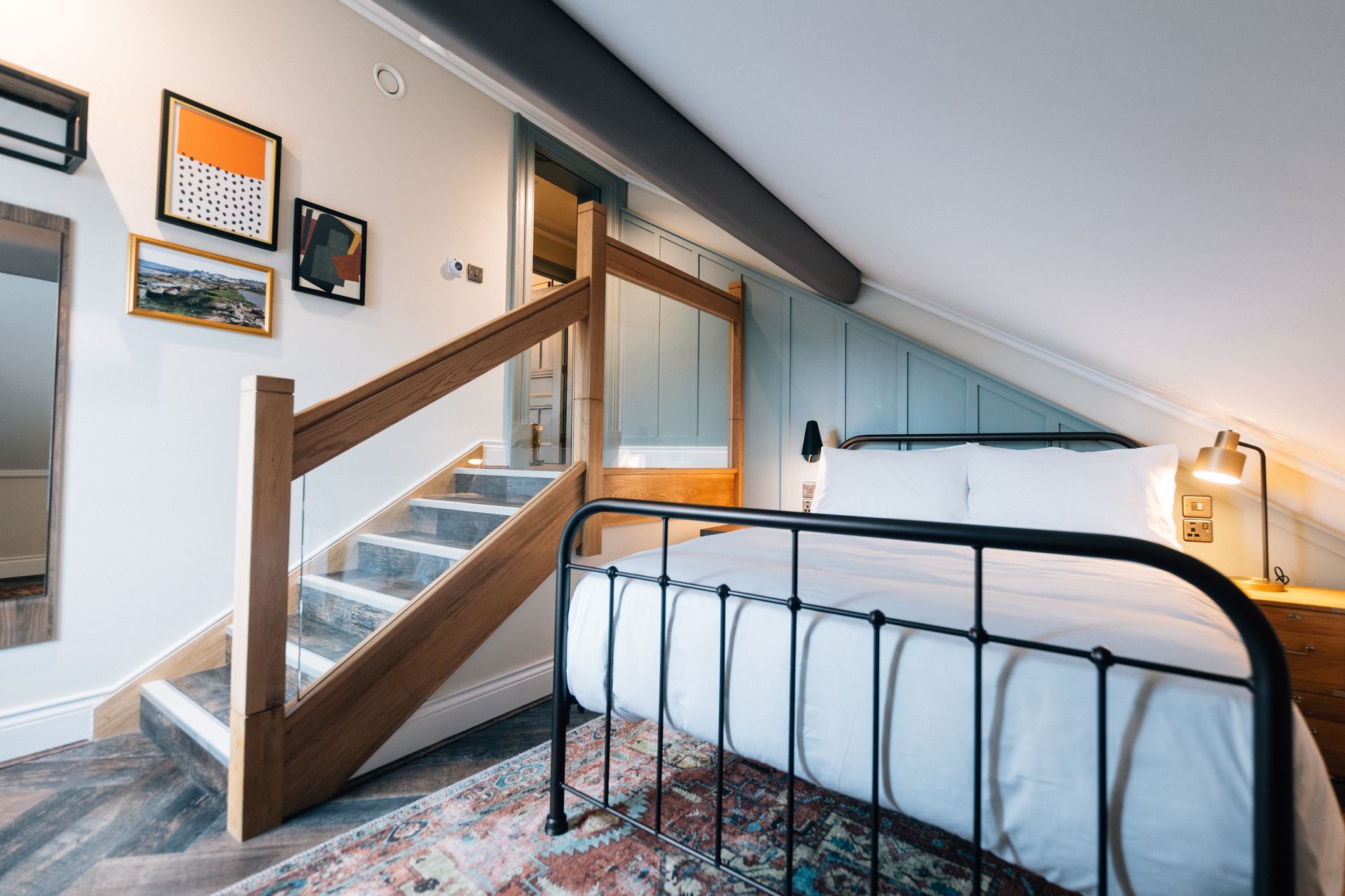 Loft bedroom with black bed, white bedding, wooden staircase, and framed wall art