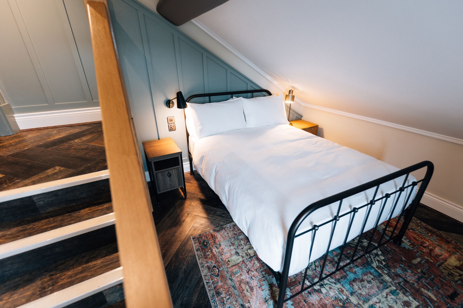 Bedroom with a bed, nightstands, and slanted blue wall. Stairs are visible to the left.
