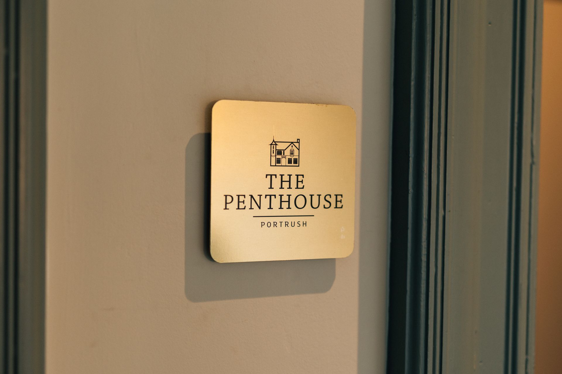 Gold plaque reading “THE PENTHOUSE” on a wall beside a blue curtain.
