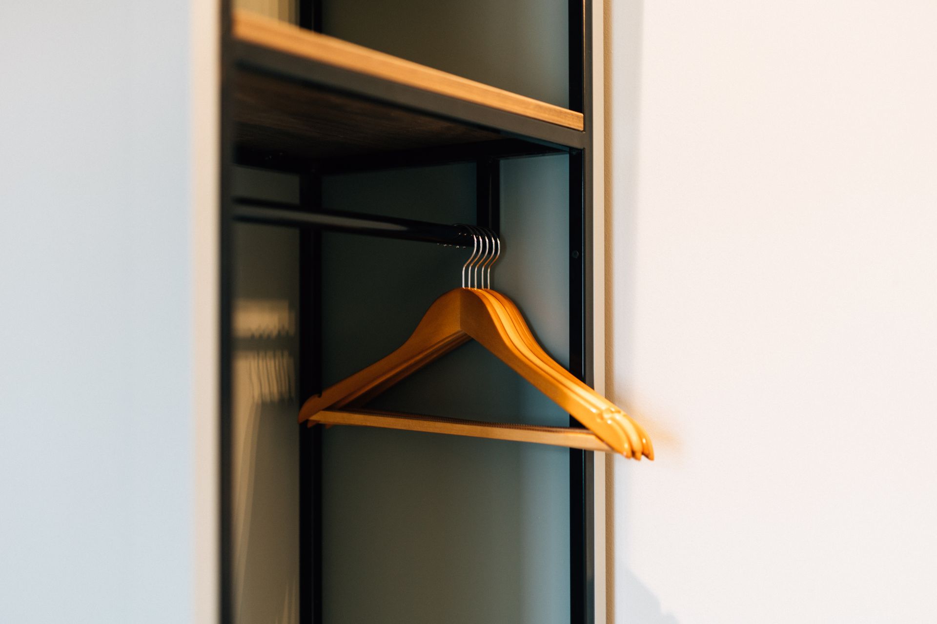 Wooden clothes hanger in an open closet with a shelf above and a white wall.