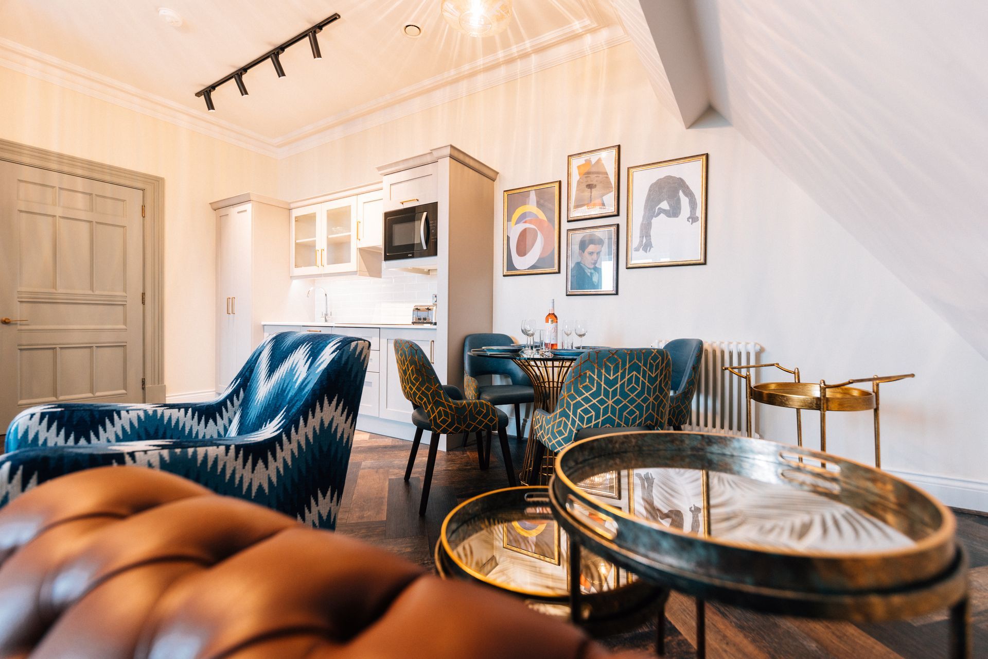 Cozy living area with a kitchenette. Features a blue patterned armchair, a leather sofa, a small dining table