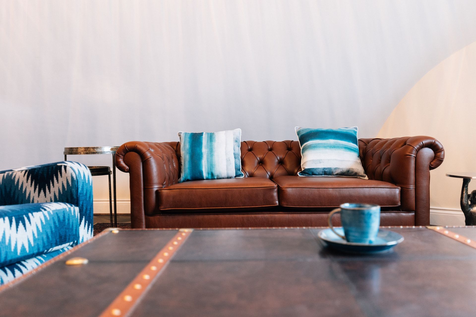 Brown leather sofa with blue-striped pillows behind a dark coffee table in a bright living room