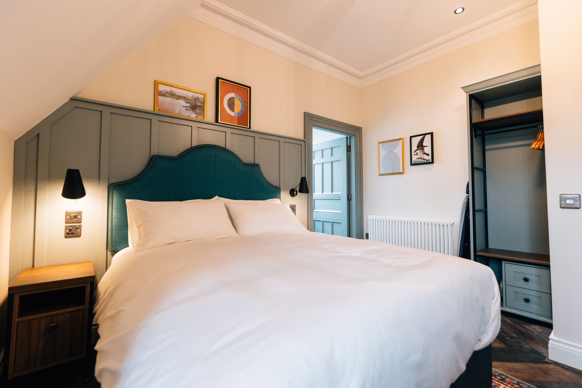 Bedroom with a large bed, teal headboard, nightstand, and artwork on the wall; a doorway and closet are also visible.