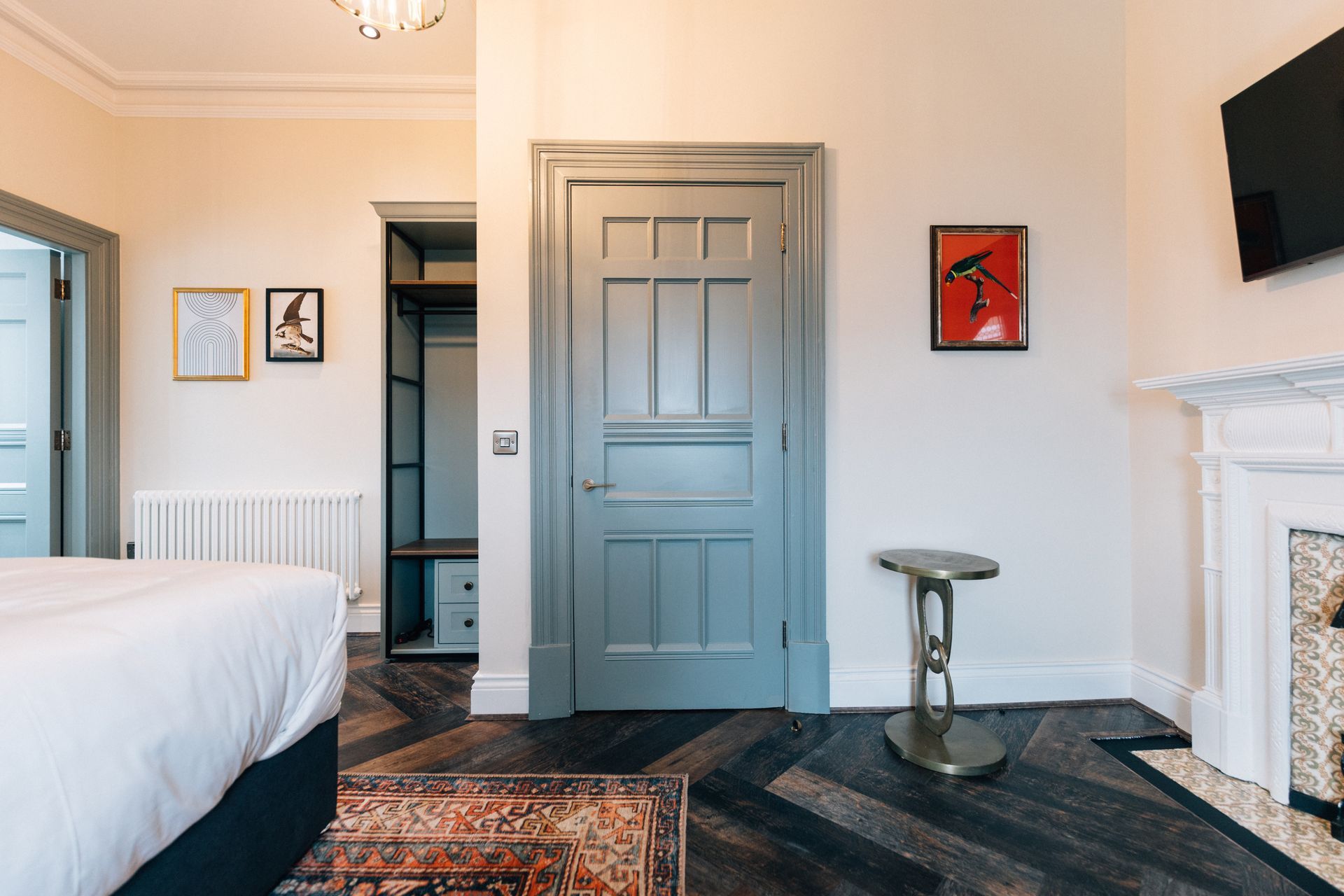 Bedroom interior with a blue door, fireplace, artwork, and herringbone wood floors. A walk-in closet is visible on the left.