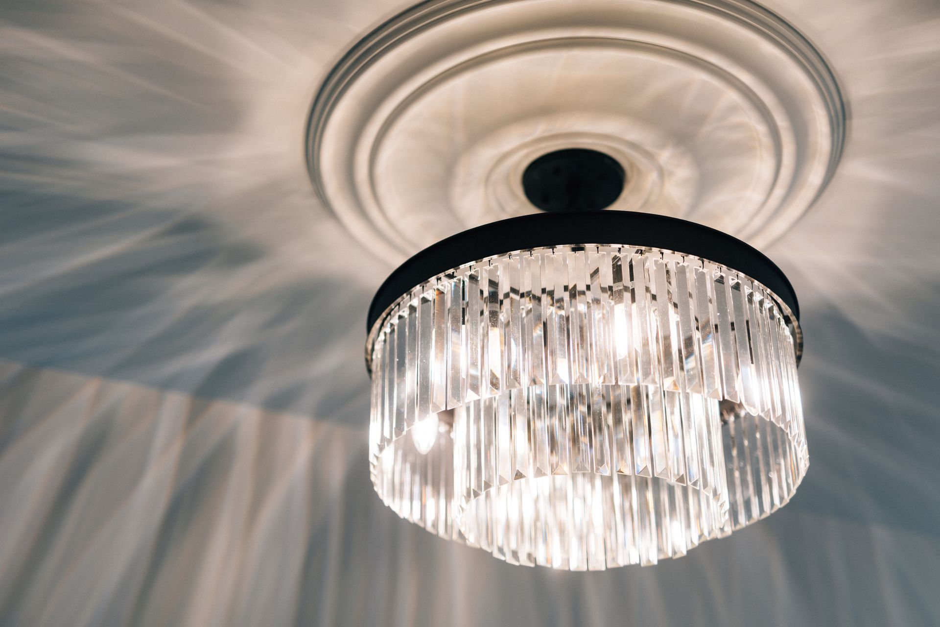 Crystal chandelier hanging from a white ceiling, casting patterned shadows.