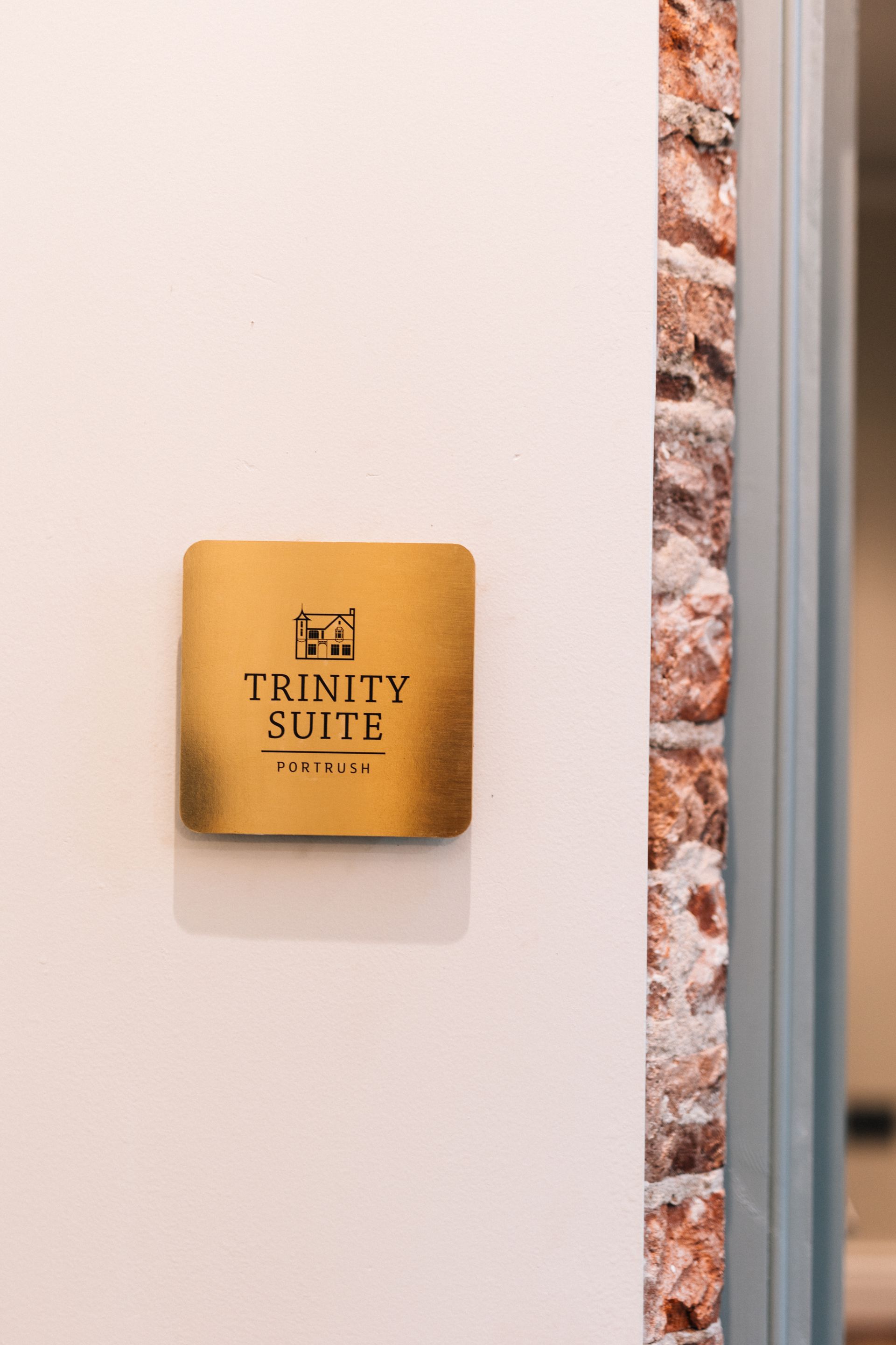 Gold “Trinity Suite” plaque on a white wall beside a stone-trimmed doorway.