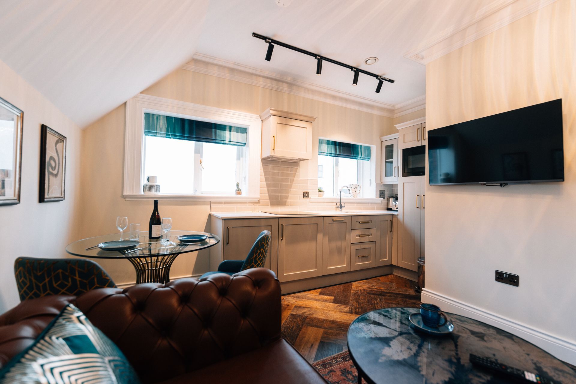 Cozy kitchen and living space in a small apartment. Features a brown leather couch, small dining table, and a kitchen 