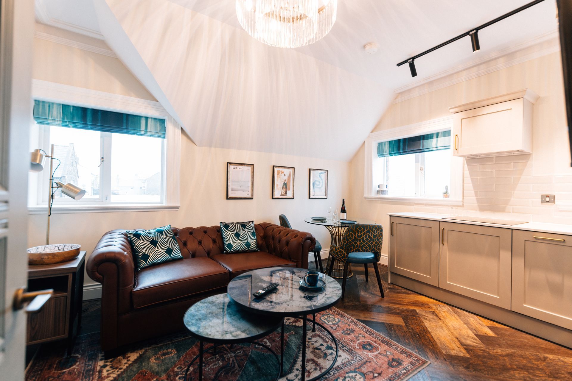 A cozy living space with a brown leather sofa, small tables, and a kitchenette. 