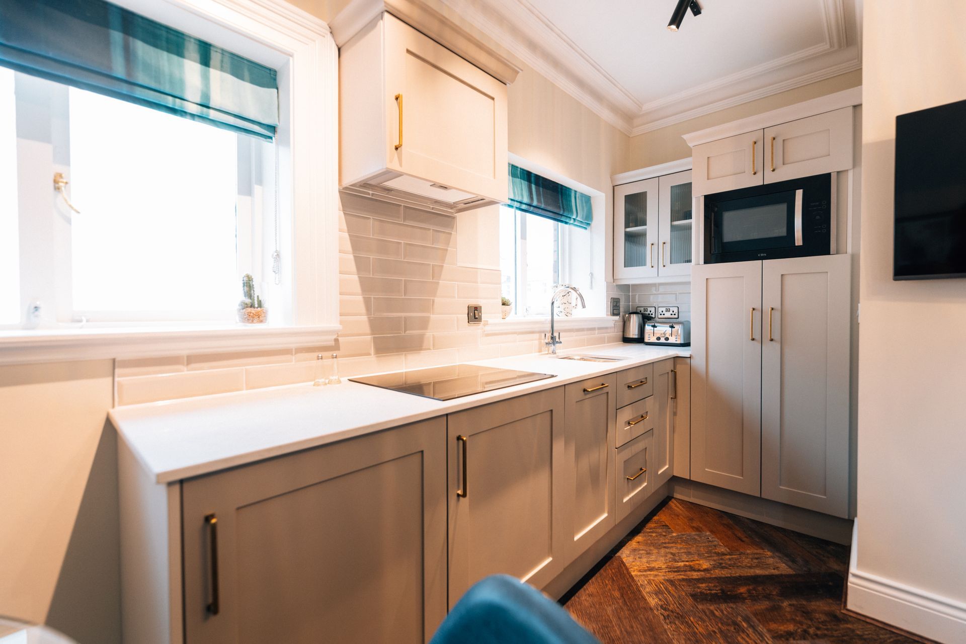 Small, bright kitchen with light cabinetry, white countertops, and a microwave. The room has a window and wood flooring.