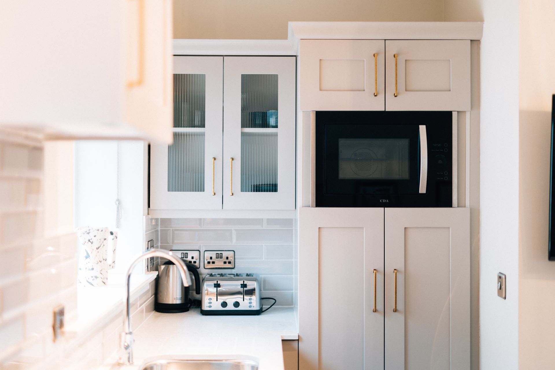 Kitchen area with white cabinets, gold hardware, and a built-in microwave.  A toaster and kettle sit on the countertop.