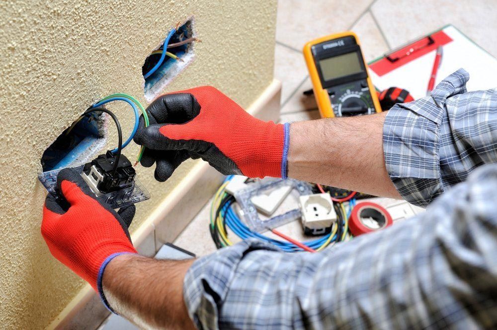 A Man Wearing Red Gloves Is Working On An Electrical Outlet — NFL Electrical In Winya, QLD
