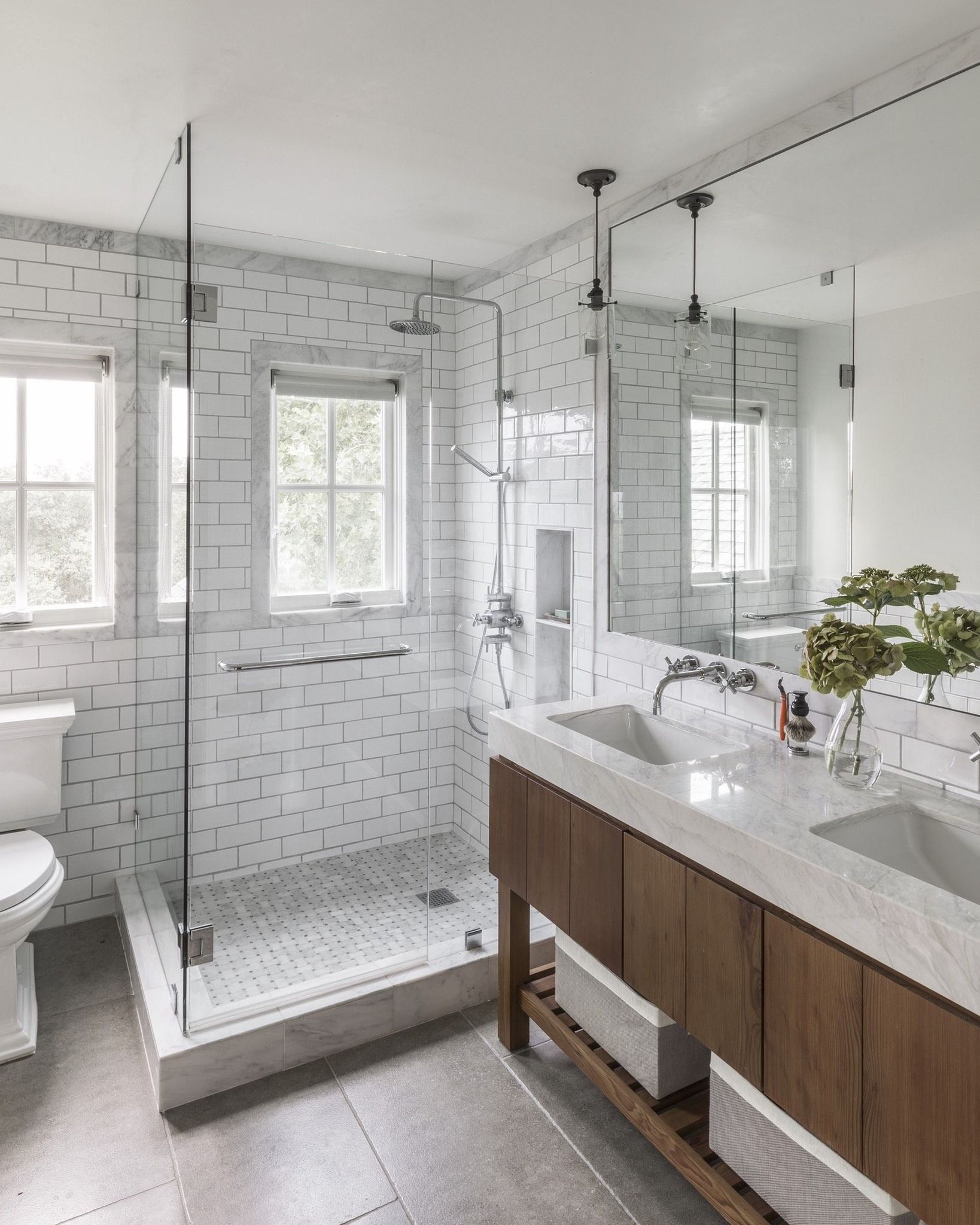 Modern bathroom with white and gray tile, glass shower, wooden vanity, and large mirror.