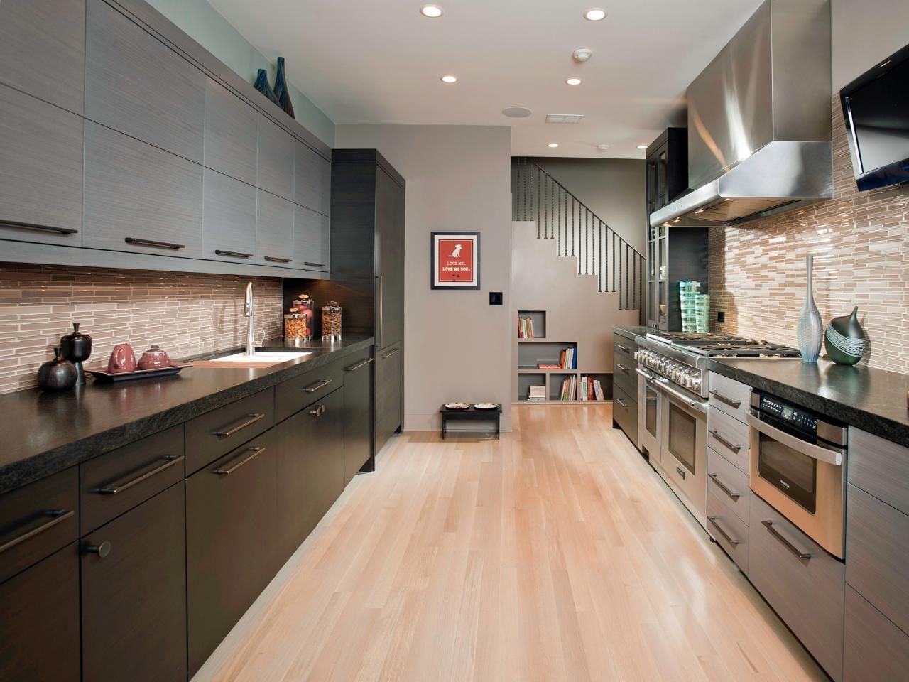 Modern kitchen with gray cabinets, stone backsplash, stainless steel appliances, and wood floor.