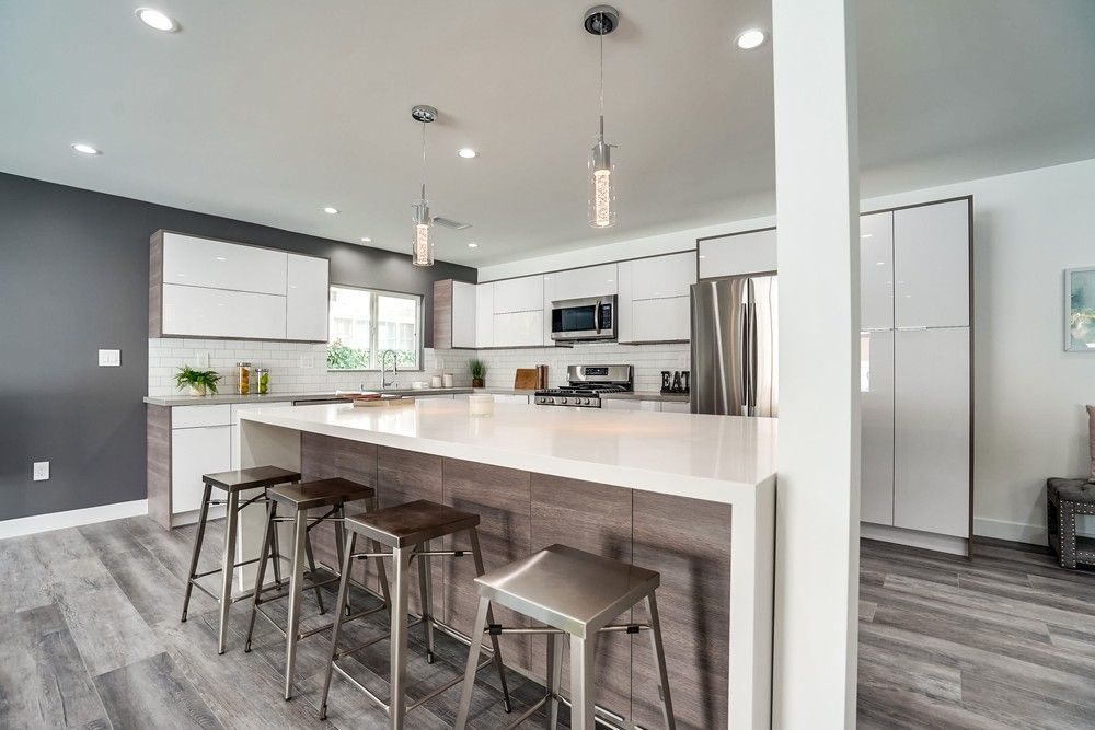 Modern kitchen with white cabinets, gray backsplash, island with stools, and stainless steel appliances.