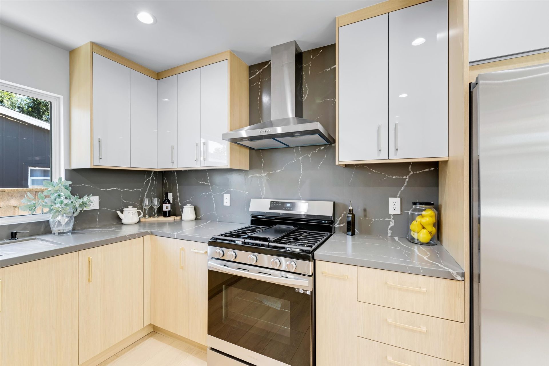 Modern kitchen with light wood cabinets, gray countertops, and stainless steel appliances.