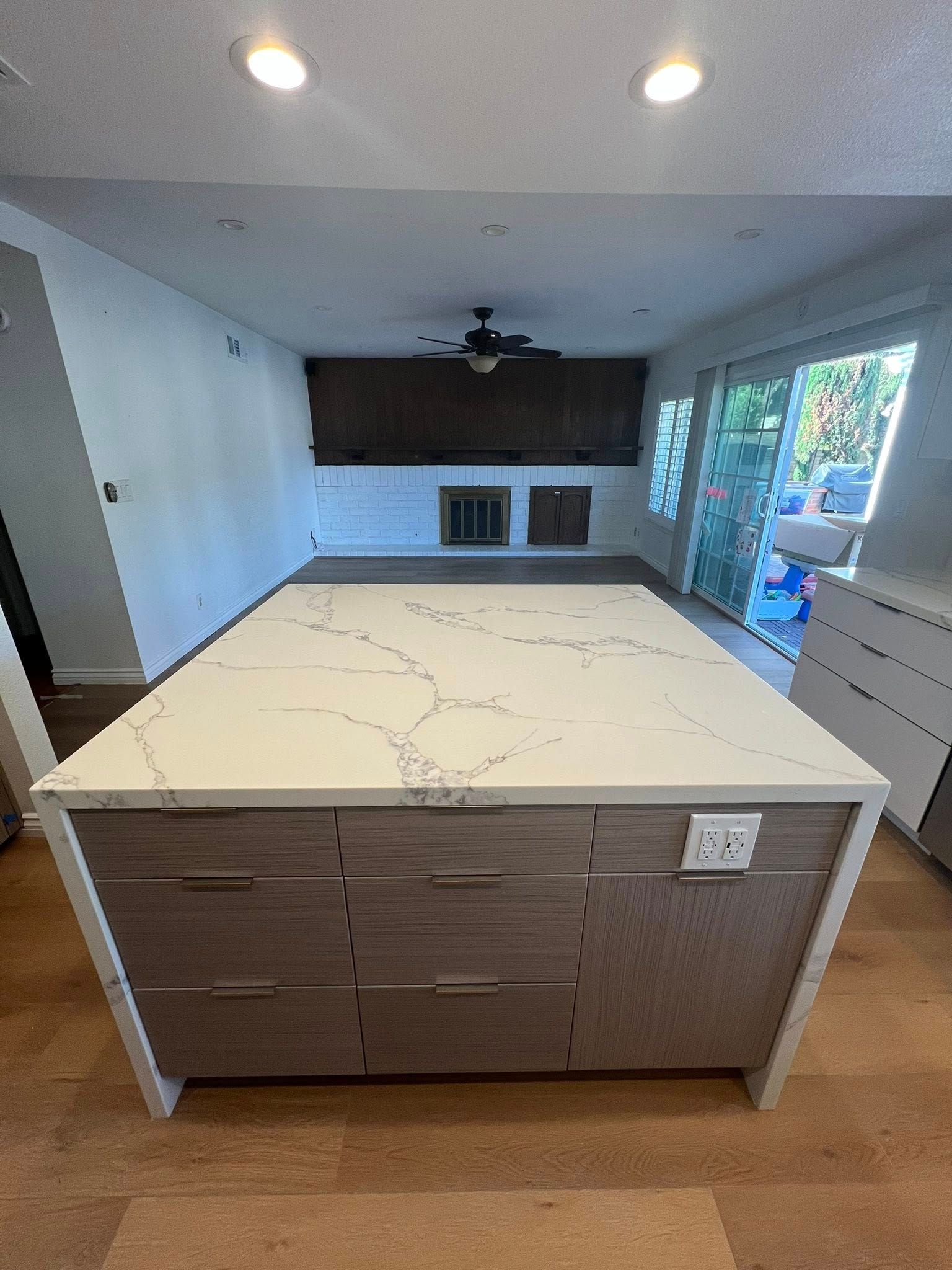 Kitchen island with quartz countertop and wood-tone cabinets; open to living area with fireplace and sliding glass door.