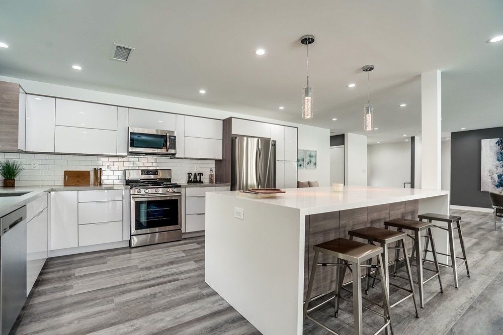 Modern kitchen with white cabinets, stainless steel appliances, large island, and grey flooring.