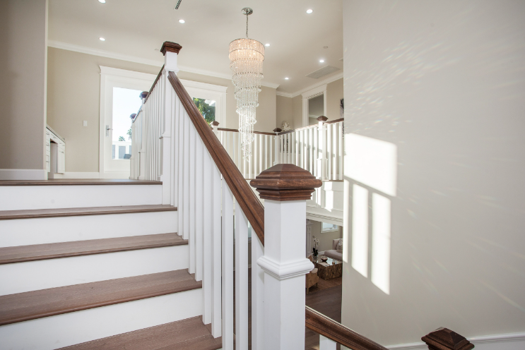 Staircase with wooden steps and white railing leading to a second floor with a chandelier.