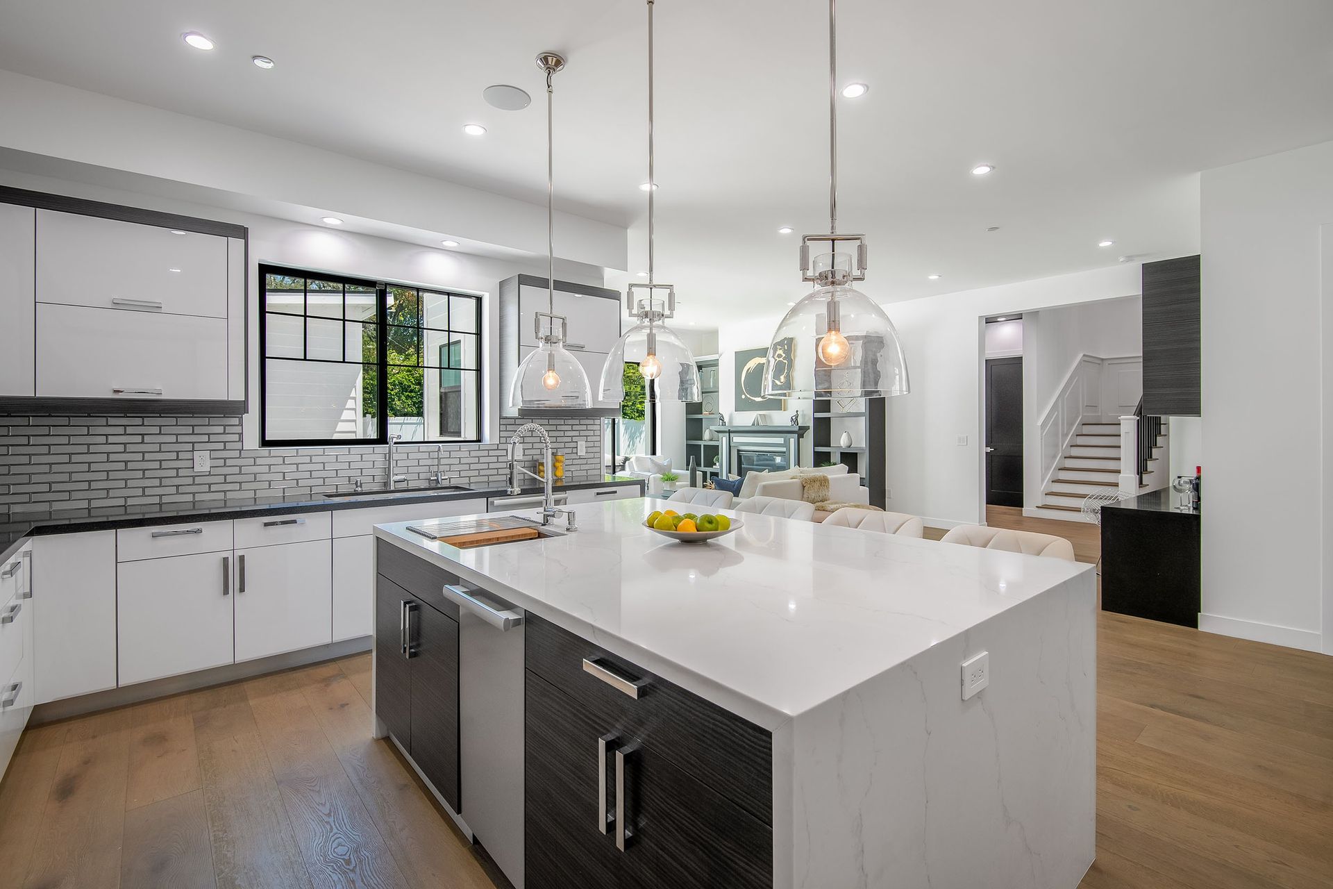 Modern kitchen with white cabinets, island, and wood floors. Sunlight streams through a window.