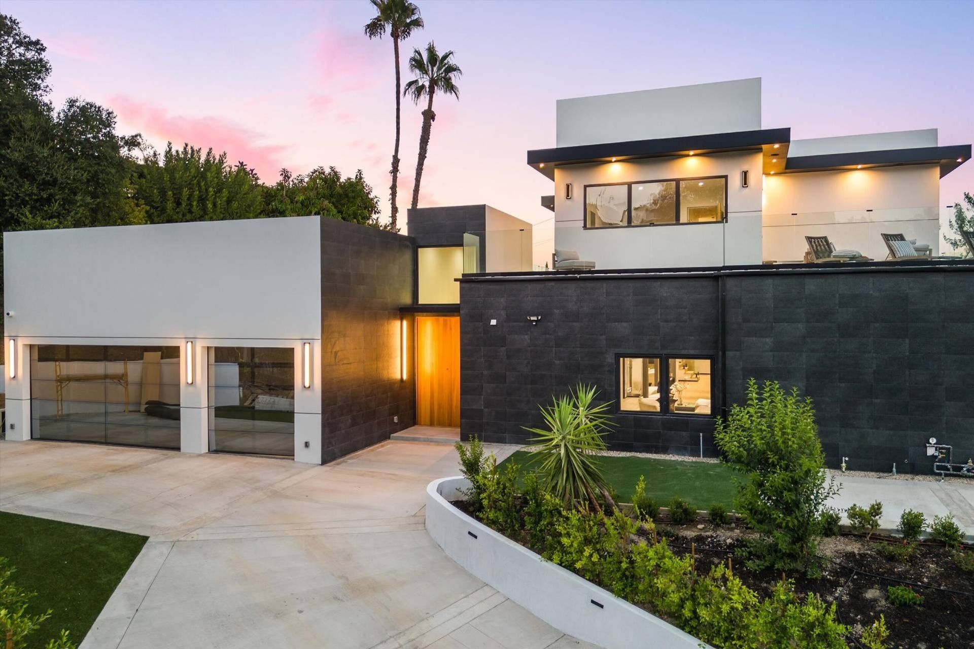 Modern home exterior with gray and white facade, glass garage doors, and palm tree.