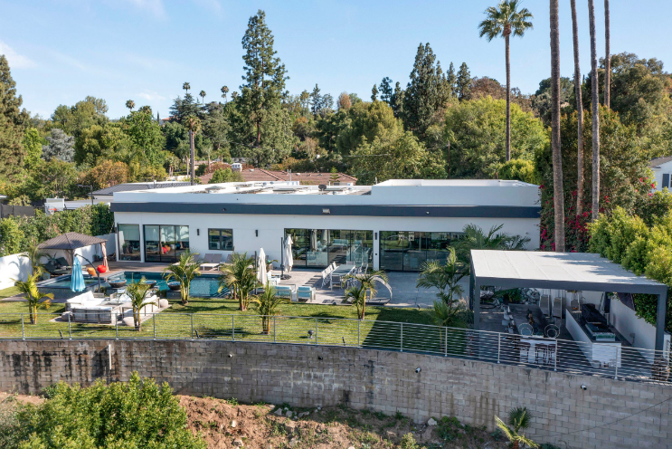 Modern home with a pool, patio, and outdoor kitchen, surrounded by trees.