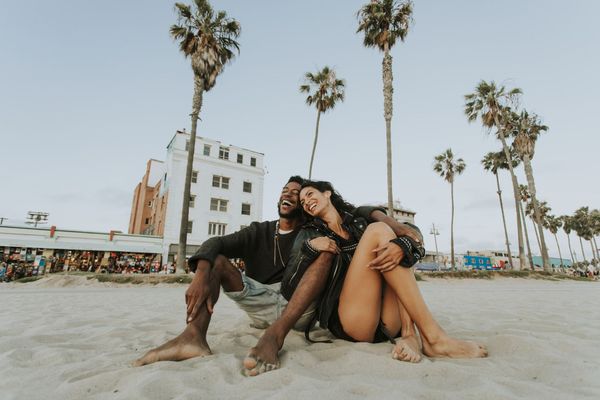 A man and a woman are sitting on the beach with palm trees in the background.