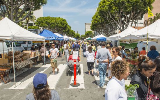 A crowd of people are walking down a street at a farmer 's market.