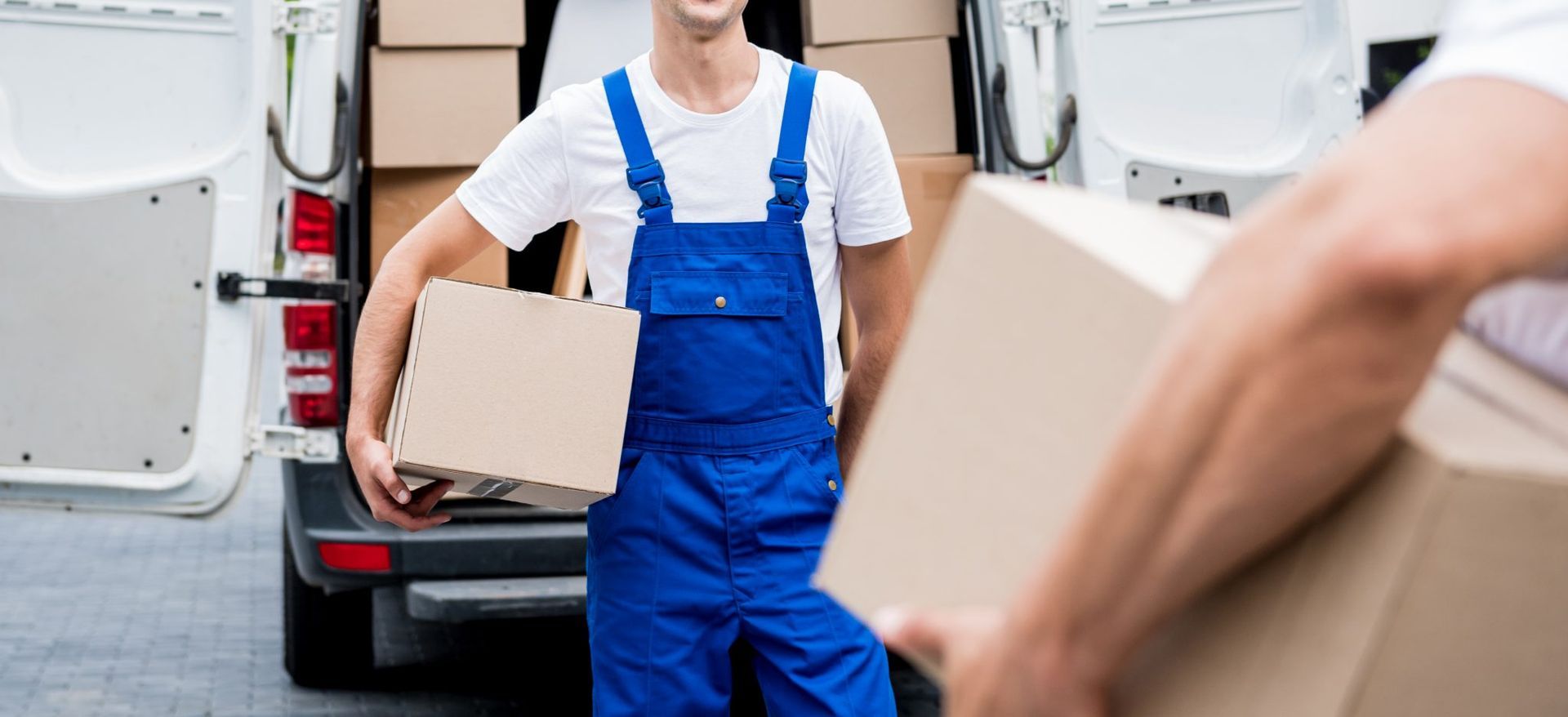 Un repartidor sostiene una caja de cartón delante de una camioneta.