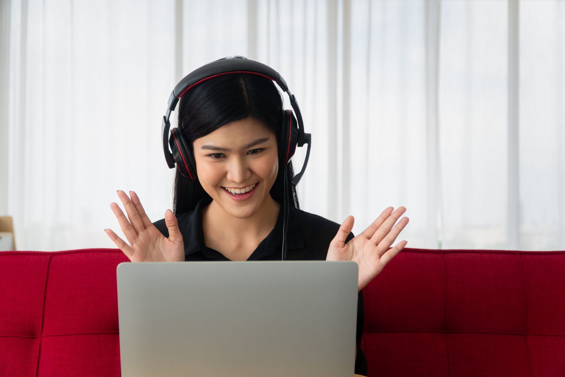 Una mujer que usa auriculares está sentada en un sofá utilizando una computadora portátil.