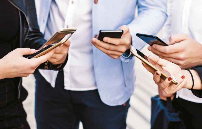 Un grupo de personas están de pie una al lado de la otra mirando sus teléfonos.