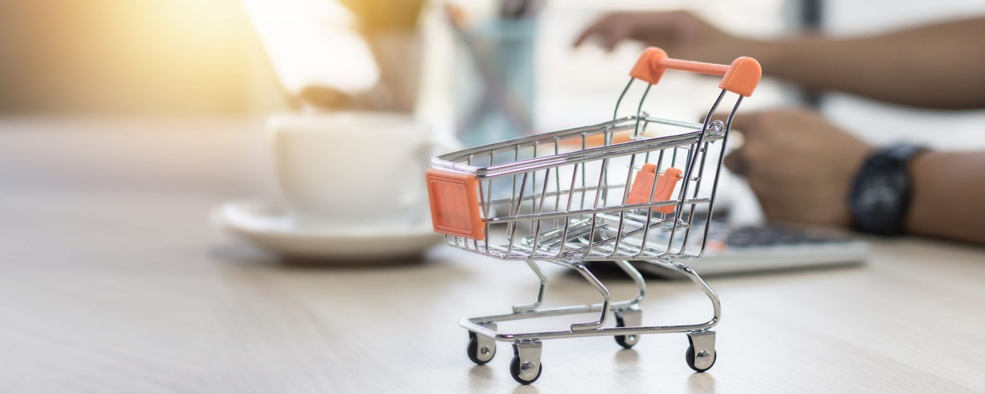 Un carrito de compras está sobre una mesa al lado de una persona que usa una computadora portátil.