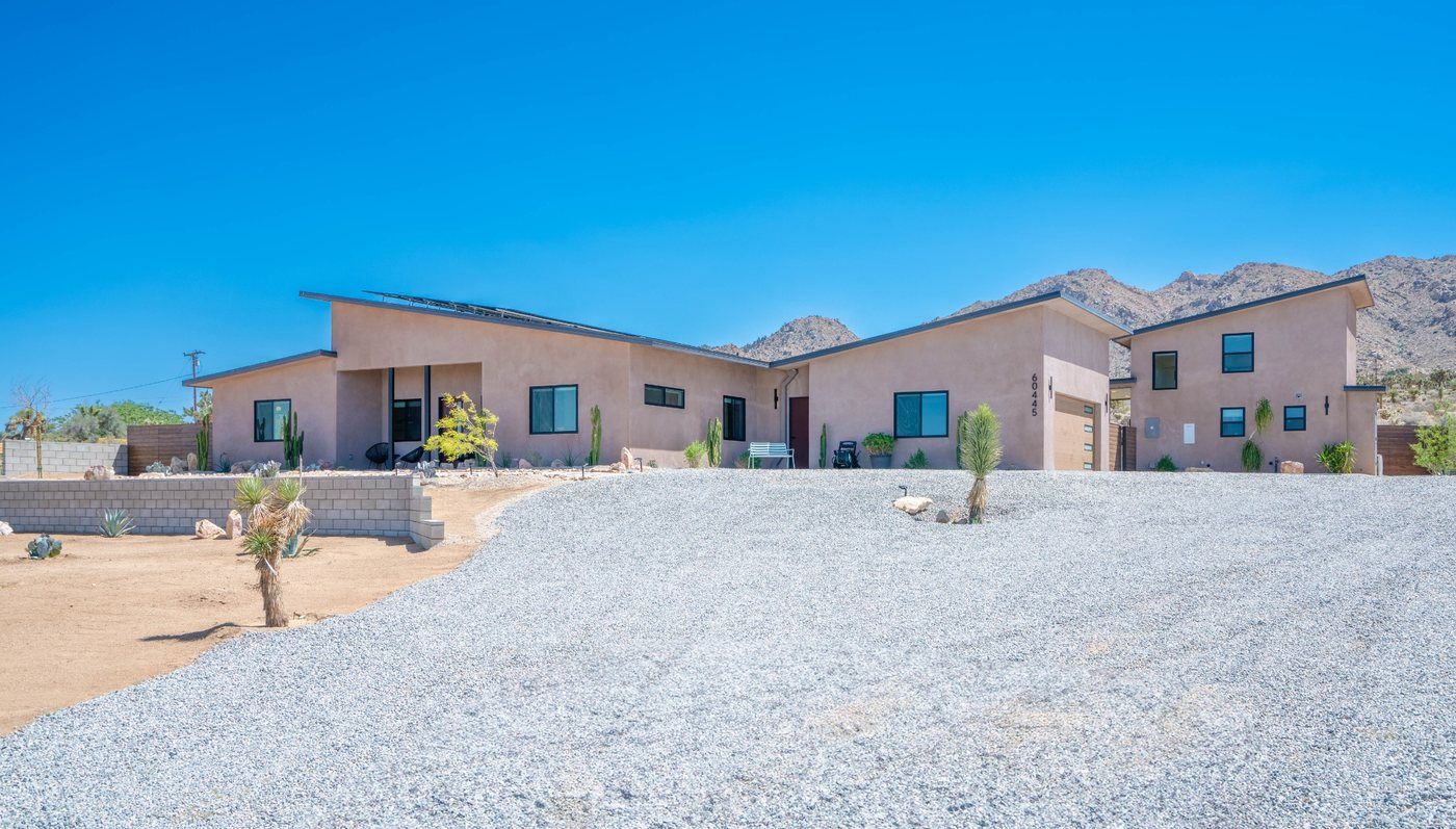 Single-story desert-style houses with tan stucco walls and a gravel front yard under a clear blue sky