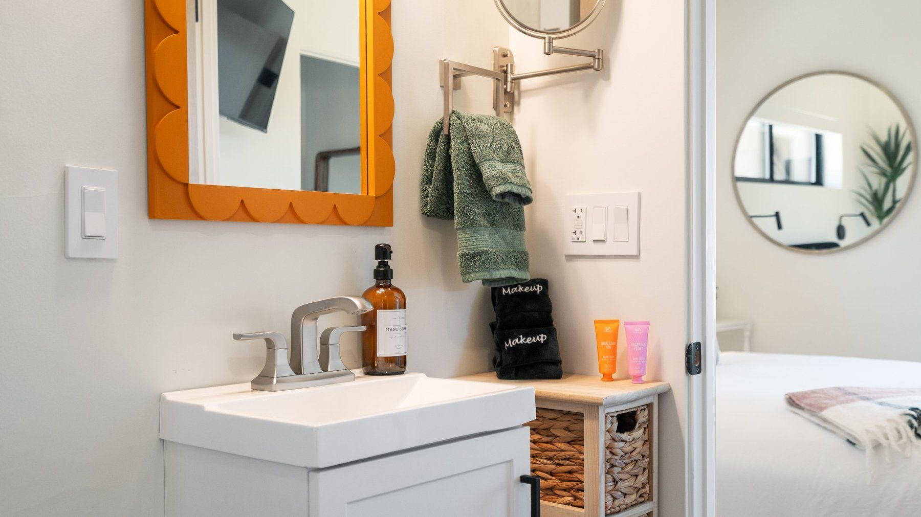 Modern bathroom vanity with orange-framed mirror, wall sconces, sink, towels, and wicker storage basket