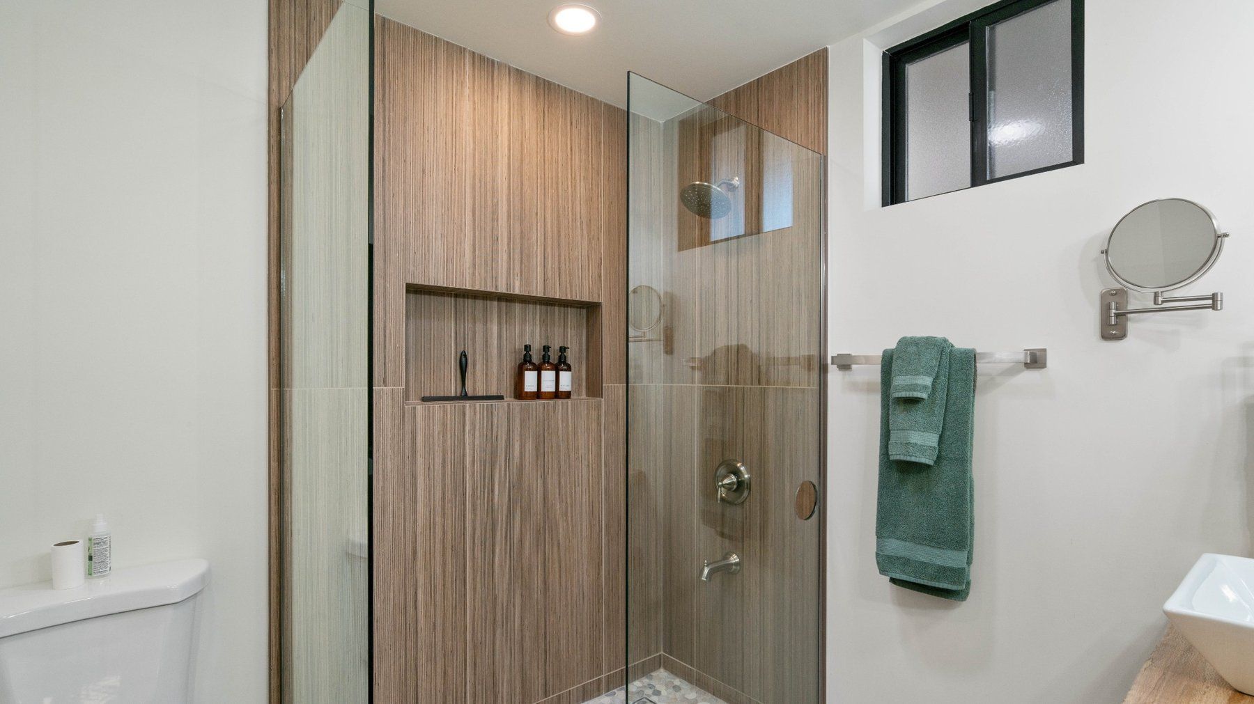 Modern bathroom shower with wood accent wall, glass enclosure, towel, and wall mirror
