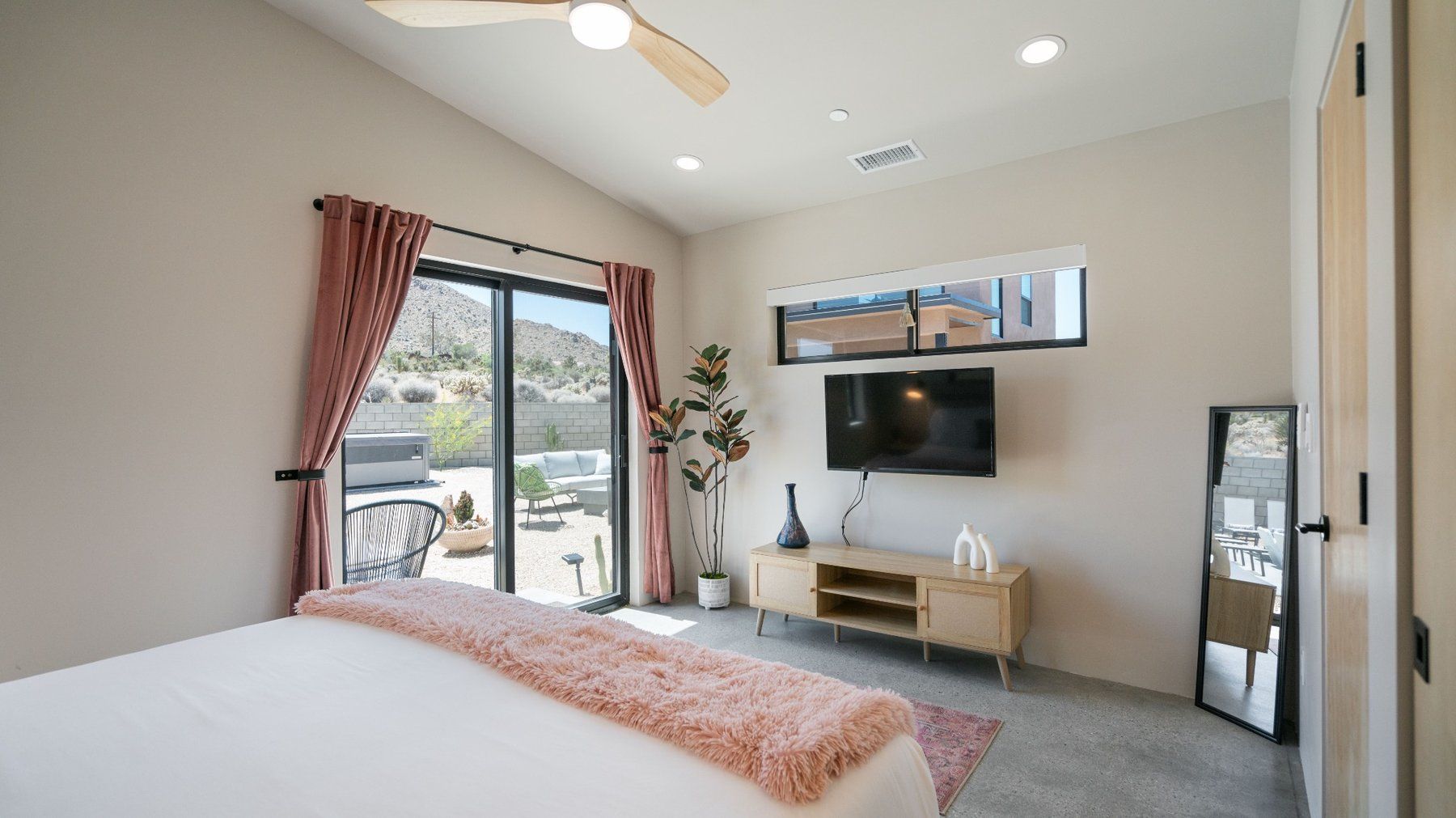 Bright bedroom with a bed, wall-mounted TV, sliding glass doors, and a small mirror near the window.