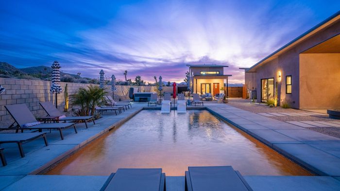 Pool with lounge chairs, desert landscape with mountains in background.
