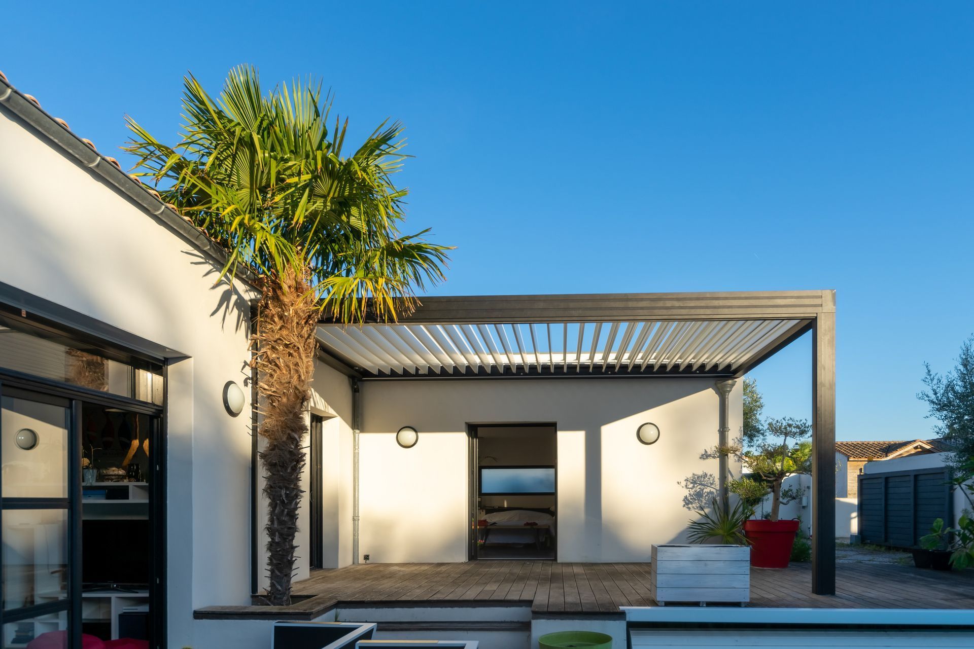 A white house with a pergola and a palm tree in front of it.