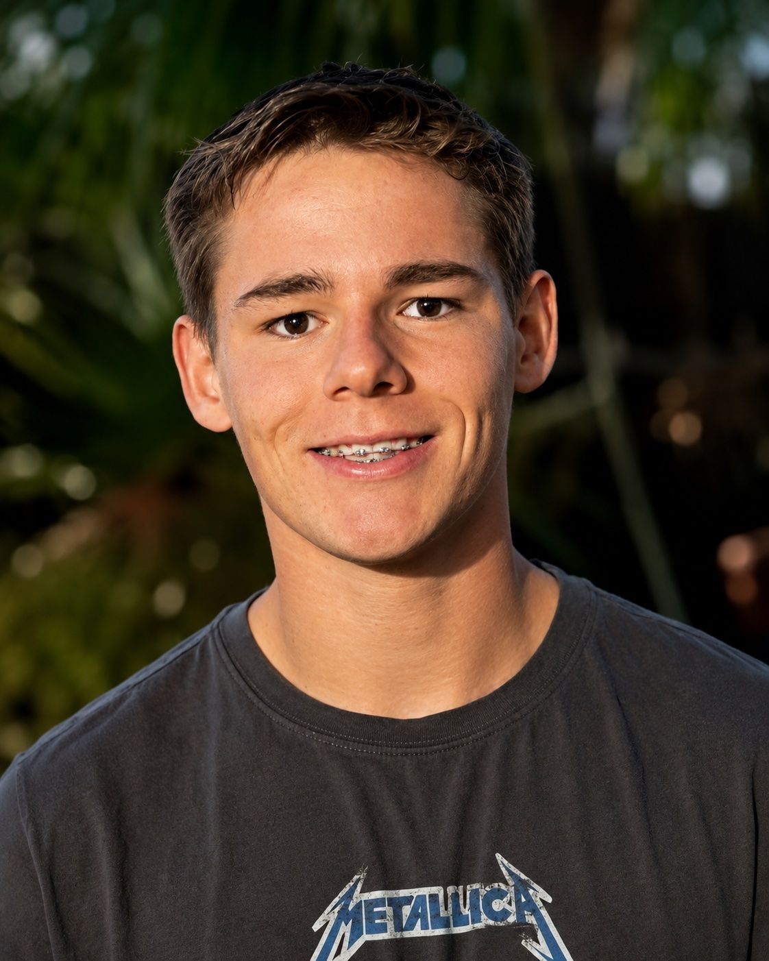 Smiling Person in a Dark Metallica T-shirt Outdoors With Blurred Greenery in the Background